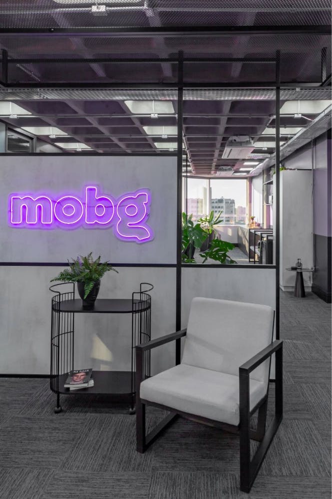 Parte do escritório da Mobg que contém uma cadeira ao lado da logo da Mobg em fluorescente